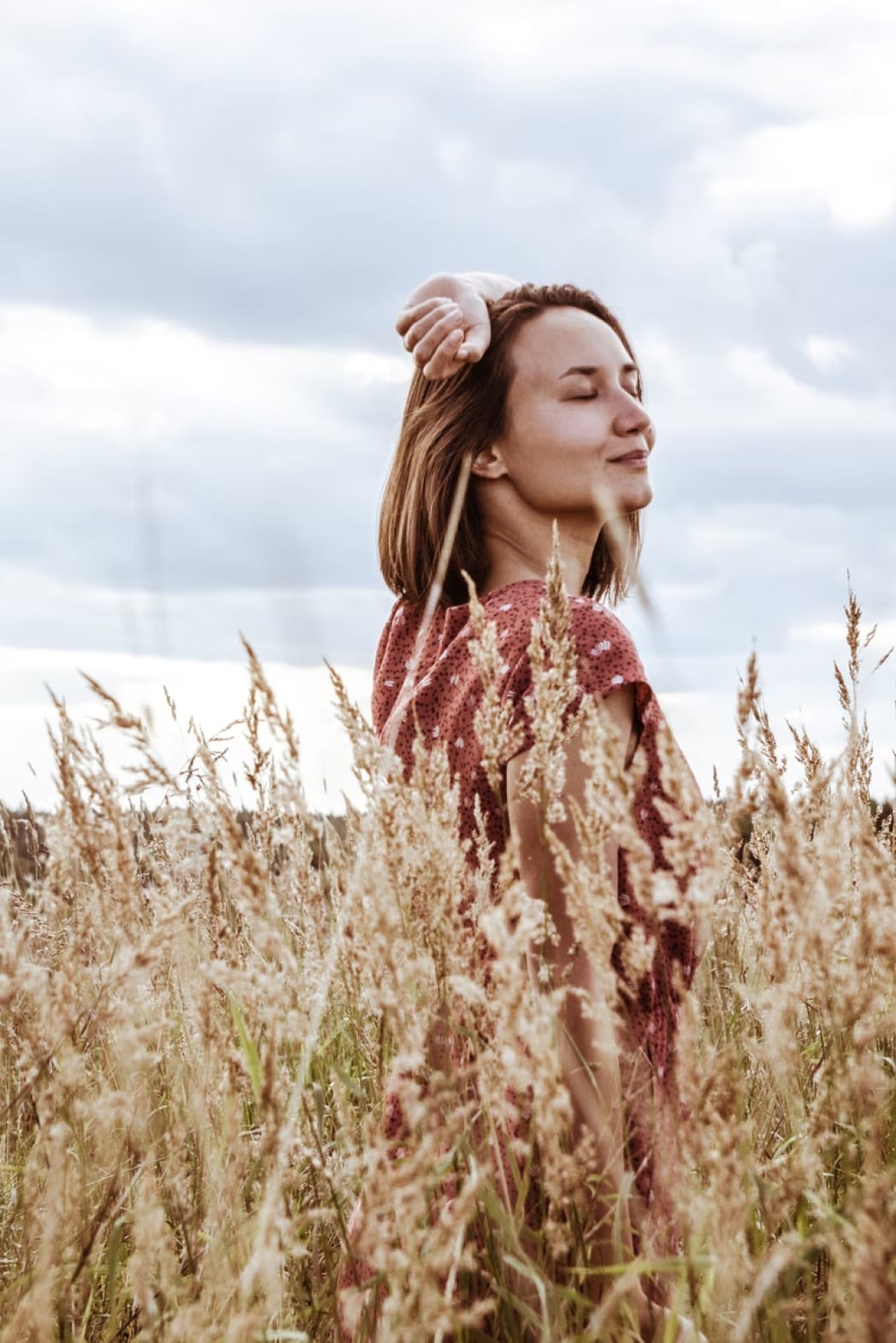 Photograph of a woman walking in the middle of a wheat field, enjoying the sunlight